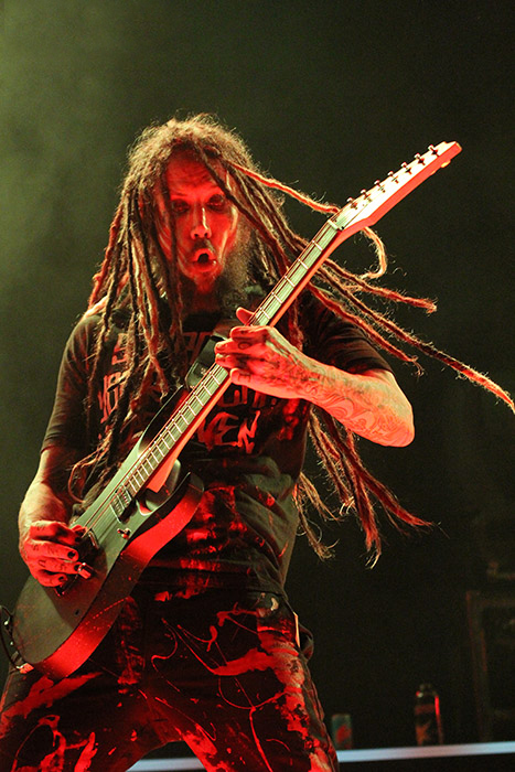 The KoRn guitarist front lit by red light against a green smoke background