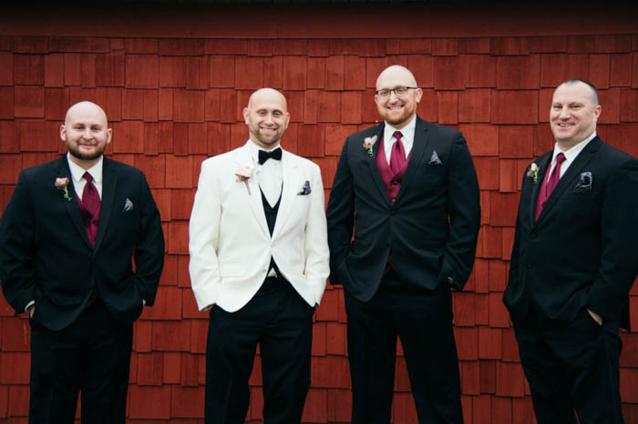 groom and groomsmen posing together with hands in their pockets against a red brick wall