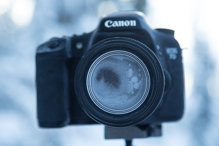 Canon camera on tripod with lens and camera body completely covered in frost, winter photography.