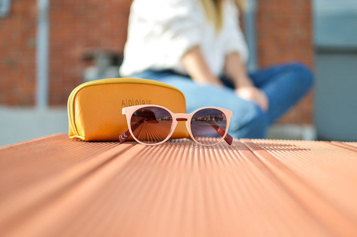 A product photography styling example of sunglasses and case on a table, with a blurry figure sitting in the background