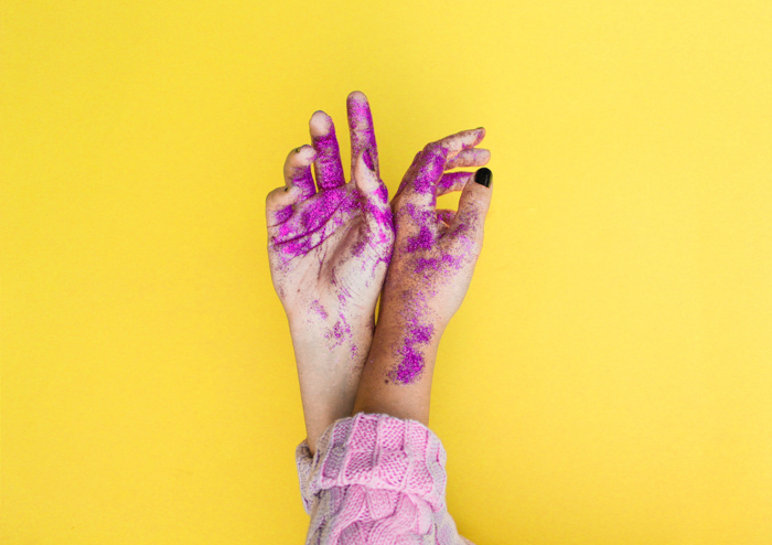 A fun image of paint and glitter covered hands featuring strong use of complementary colors yellow and purple 