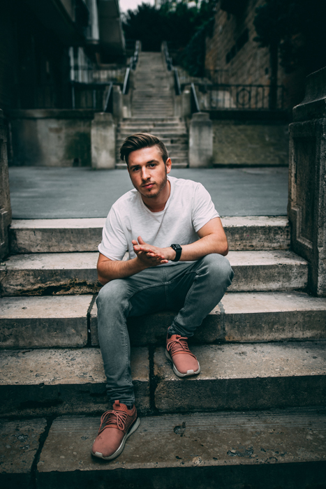 A male model posing casually outdoors on stone steps